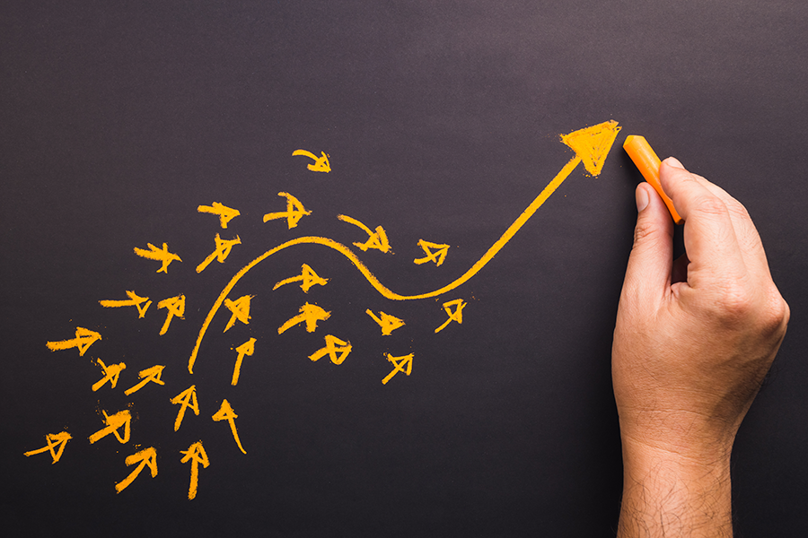 Hand drawing a large yellow arrow curving upward on a blackboard with many smaller arrows pointing toward it.